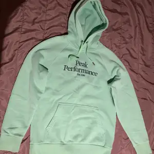 Säljer en superfräsch mintgrön hoodie från Peak Performance. Den har en klassisk design med en stor ficka fram och justerbar huva. Perfekt för både chill och aktivitet. Den är i storlek S och i riktigt bra skick. Perfekt för höst och vår!