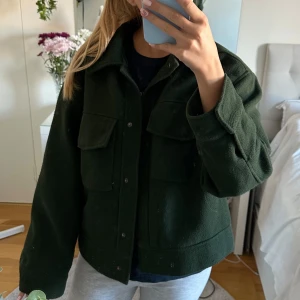 Mörkgrön jacka från Monki - Säljer en snygg mörkgrön jacka från Monki i storlek M. Jackan har en cool och avslappnad stil med stora fickor framtill och knappar. Perfekt för höst och vår! 💚