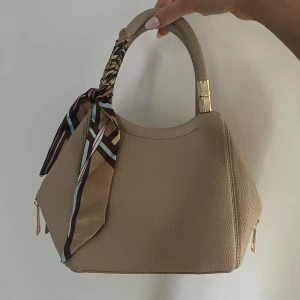 Beige handväska - Säljer denna jätte fina och eleganta väskan då jag har jätte många väskor och just denna har aldrig kommit till användning! Den är köpt i Spanien💞 Man får även med ett axelremsband!