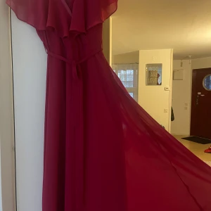 Röd långklänning  - Elegant mörkröd långklänning med volangdetaljer och v-ringning. Klänningen har ett knytband i midjan som ger en smickrande passform. Perfekt för speciella tillfällen. Köpt utomlands så storleken passar inte med lappen, hade sagt att det är storlek M. Priset går att diskutera! 