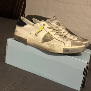 Vita sneakers från Philippe Model - Snygga vita sneakers från Philippe Model med grå och svarta detaljer. Skorna har en unik design med gul snörning och en robust sula. Perfekta för en avslappnad stil. På ena inne sidan av skon har det lossnat, märker dock inte med skon på!