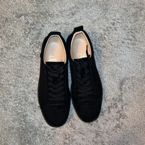 Svarta sneakers från Christian Louboutin - Snygga svarta sneakers i mocka från Christian Louboutin med den ikoniska röda sulan. Skorna har snörning och en stilren design som passar perfekt för en trendig look. De är använda 2 gånger men är som nya ungefär. Jag säljer dessa för att de är lite stora