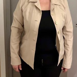 Beige kavaj från Vero Moda - Snygg beige kavaj från Vero Moda med knappar framtill. Perfekt för en stilren look. Kavajen har en klassisk krage och långa ärmar.