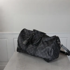 Louis Vuitton Keepall 55 Monogram Eclipse - Snygg svart väska från Louis Vuitton med det klassiska monogrammönstret. Väskan har en dragkedja och avtagbar axelrem för extra bekvämlighet. Perfekt för resor med stil. Denna är den största storleken alltså 55cm och är endast använd en eller två gånger sen den köptes in 2021. Inga skavanker eller skador. Som ny.