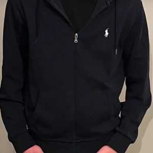   Ralph Lauren - Snygg mörkblå  hoodie från Ralph Lauren med dragkedja och klassisk logga på bröstet. Perfekt för en avslappnad stil med justerbar huva och fickor framtill. Fåtal gånger använt. Säljer den tack vare den är lite för stor. Inga defekter! Skriv om ni har frågor! Storlek M. kan gå ner i pris vid snabb affär! Köpt för ungefär 2100.