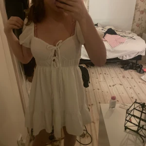 Vit kortklänning med volangdetaljer - Så så fin vit kortklänning med volangdetaljer och knytning framtill!💗 Klänningen har bara blivit använd vid 2 tillfällen!!