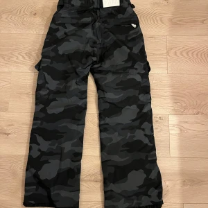 Camouflage termobyxor / täck byxor  - Snygga termobyxor / täck byxor i svart och grått camouflage. Byxorna har en loose passform med flera praktiska fickor och dragkedja. Perfekta för en avslappnad stil. Bra skick. 