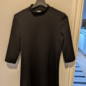Svart klänning med trekvartsärm - Svart klänning med trekvartsärm.. Klänningen har en liten öppning i ryggen som ger en extra detalj. Perfekt för en stilren look.