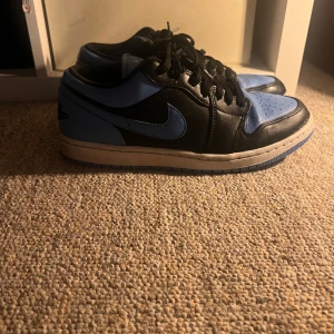 Nike Air Jordans i svart och blått - Snygga Nike Air Jordans i svart och blått med klassisk snörning. Skorna har en stilren design med en kontrasterande vit sula. Perfekta för dig som vill ha en sportig look med en touch av stil.