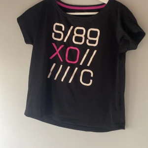 Svart t-shirt med tryck - Säljer en svart t-shirt med ett coolt tryck i vitt och rosa på framsidan. T-shirten har korta ärmar och en rund halsringning. Perfekt för en avslappnad stil.