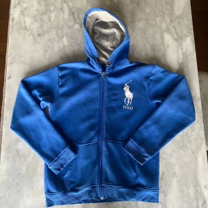 Blå Ralph Lauren zip tröja  - Skick: 7/10. Tröjan är i bra skick förutom en liten fläck på en av fickorna framtill (se bild 5). Från märket Ralph Lauren och i storlek M men skulle också passa S. Om du är osäker på om det kommer att passa kan du alltid fråga om mått!
