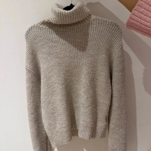 Beige stickad polotröja från H&M - Mysig beige stickad polotröja från H&M i storlek XS. Perfekt för kyliga dagar med sin höga krage och långa ärmar. Tröjan är tillverkad i en mjuk polyesterblandning som ger en skön känsla mot huden.