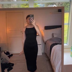 Svart långklänning med smala axelband - Elegant svart långklänning med smala axelband och  randigt mönster. Perfekt för en stilren look. Klänningen är tajt och framhäver dina former!