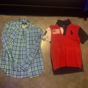 Röd pikétröja och blå rutig skjorta från Ralph Lauren - Säljer en röd pikétröja med amerikansk flagga och en blå rutig skjorta från Ralph Lauren. Pikétröjan har korta ärmar och en klassisk krage, medan skjortan är långärmad med knappar framtill. Perfekt för en stilren look! Tveka inte att höras av vid intresse😁
