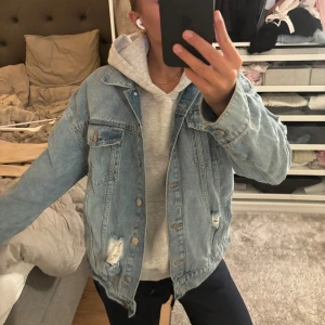 Ljusblå jeansjacka - Säljer en klassisk ljusblå jeansjacka med slitna detaljer. Jackan har knappar framtill och två bröstfickor med lock. Perfekt för en avslappnad stil.