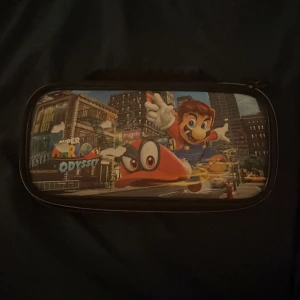 Nintendo Switch-väska med Super Mario Odyssey-motiv - Säljer en nintendo switch väska, har använt 10-15 gånger och bilden på väskan är lite riven. Men funkar helt perfekt och kan bära runt din nintendo vart du än går och är lätt att bära. Priset kan diskuteras👍🏼☺️