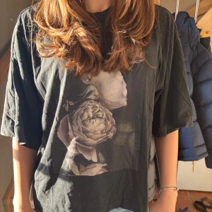 Svart t-shirt med blommotiv - Säljer en svart t-shirt med ett vackert blommotiv i dämpade färger. 