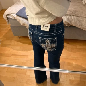 Lågmidjade mörkblå jeans med broderade detaljer - Snygga mörkblå jeans med unika broderade detaljer på bakfickorna. Jeansen har en klassisk passform med vita sömmar som ger en cool kontrast. Perfekta för dig som vill ha något extra i garderoben!