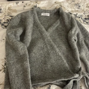 SÄNKT PRIS Grå populär knytkofta  - En populär mysig grå omlottkofta från Design by Amor i storlek XS. Koftan har långa ärmar och knytband i midjan för en justerbar passform. Perfekt för kyliga dagar. Inte min storlek tyvärr så har aldrig använt.