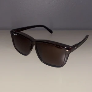 Solglasögon från Ray-Ban - Snygga solglasögon från Ray-Ban med en klassisk design. Bågarna är i en mörkbrun nyans och har en stilren form. Perfekta för att ge en cool touch till din stil. Box saknas tyvärr därav priset. Fick de i present men passade inte riktigt min stil. Glajorna är mörkbruna. Skriv för fler bilder eller frågor.