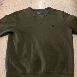 Olivgrön tröja från Polo Ralph Lauren - Säljer en stilren olivgrön tröja från Polo Ralph Lauren. Tröjan har en diskret logga på bröstet och är tillverkad i ett mjukt material. Perfekt för en avslappnad look.