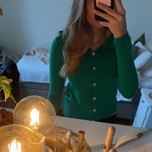 Grön kofta med volangkrage - Säljer en snygg grön kofta från Fashion med volangdetaljer vid kragen och knappar framtill.  I storlek L/XL men är väldigt små i storleken och sitter tight på mig som vanligtvis är S. Pris kan diskuteras. Säljer en likadan i svart om man är intresserad.