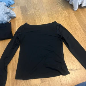 Svart långärmad topp - Säljer en stilren svart långärmad topp med en elegant offshoulder-design. Perfekt för att skapa en chic look. Passar bra till både jeans och kjol.