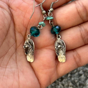 Örhängen med turkosa pärlor och silverdetaljer - Unika örhängen med turkosa och mörkblå pärlor samt detaljer i silver. Designen inkluderar små sandalliknande hängen med blommönster. Perfekta för att ge en bohemisk touch till din stil.