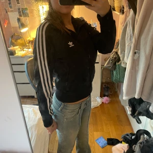 Svart träningsjacka från Adidas - Säljer en svart träningsjacka från Adidas med de klassiska tre vita ränderna längs ärmarna. Jackan har dragkedja framtill och Adidas-loggan på bröstet. aldrig använd!💕