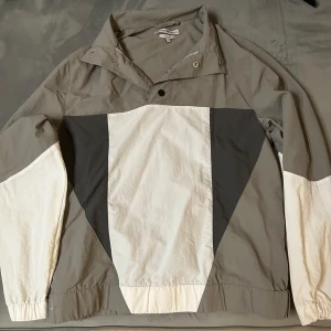 Grå och vit jacka från Another Influence - Säljer en stilren jacka från Another Influence i grått och vitt. Jackan har en unik design med blockmönster och knappar vid kragen. Perfekt för en avslappnad look.