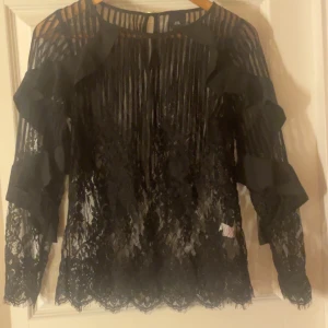 Svart spetsblus med volanger - Elegant svart spetsblus med långa ärmar 