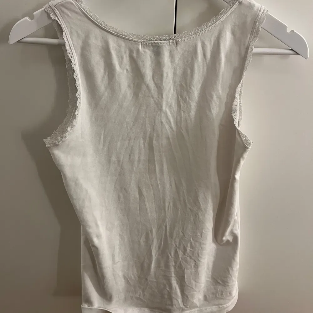 Säljer en stilren vit linnetopp med fina spetsdetaljer längs halsringningen och ärmhålen. Perfekt för en enkel och fräsch look. Passar bra till både jeans och kjol.. Yläosat.
