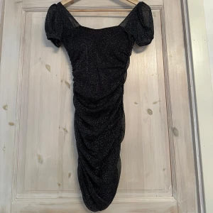 Svart glittrig klänning - Snygg svart glittrig klänning med korta puffärmar och en rynkad design. Perfekt för festliga tillfällen. Passar xs/s.