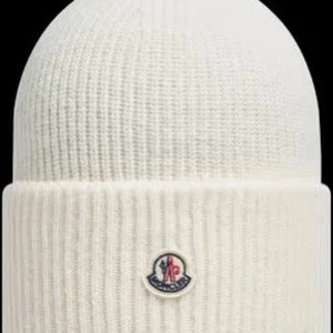 Vit stickad mössa från Moncler - Snygg vit stickad mössa från Moncler med ribbad design och deras ikoniska logga framtill. Perfekt för att hålla värmen under kyliga dagar.de är en replika men den är otroligt lik❤️