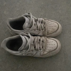 Nike Air Force  - Säljer ett par vita sneakers med snörning. Skorna har en klassisk design med perforerade detaljer på ovansidan för ventilation. Perfekta för en avslappnad stil.