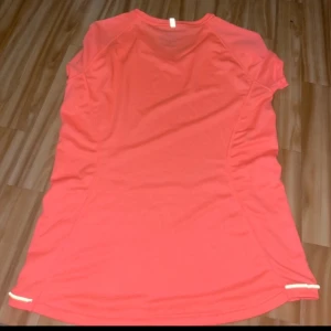 Neon rosa träningstopp från Ravelli - Säljer en neon rosa  träningstopp från Ravelli i storlek M. Toppen är kortärmad och har en v-ringad design. Perfekt för träning med sitt lätta och bekväma polyester-material.