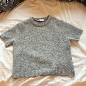 Grå kortärmad tröja från Zara - Säljer en stilren grå tröja från Zara. Den är kortärmad och har en rund halsringning. Perfekt för en avslappnad look.