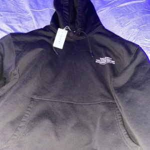 Svart hoodie från Vailent  - Snygg svart hoodie från Vailent med en liten vit logga på bröstet. Den har en klassisk design med en stor ficka framtill och justerbar huva med snören. Perfekt för en stilren och bekväm look. Nypris 800kr helt ny lappen sitter kvar