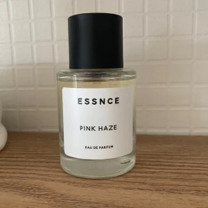 Essnce Pink Haze Eau de Parfum - Säljer en flaska Essnce Pink Haze Eau de Parfum. Flaskan är genomskinlig med en enkel vit etikett och har en stilren svart kork. Perfekt för den som gillar en subtil och elegant doft.