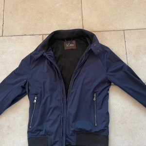 Mörkblå jacka från Oscar Jacobson - Snygg mörkblå jacka från Oscar Jacobson med dragkedja och krage. Perfekt för en stilren look i vår. Jackan har praktiska fickor med dragkedjor och en diskret design. 