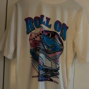 Vit t-shirt med tryck - Cool vit t-shirt med ett färgglatt tryck på baksidan. Trycket visar en blå bil, rosa tärningar och texten 'Roll On' i blått och lila. 