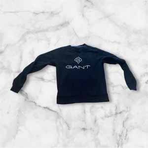 Svart sweatshirt från GANT - Säljer en stilren svart sweatshirt från GANT med deras logga tryckt på framsidan. Tröjan har långa ärmar och en klassisk rund halsringning. Perfekt för en avslappnad stil.