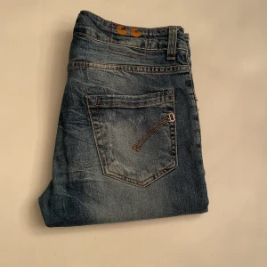 Blå jeans med slitningar - Snygga blå jeans med coola slitningar från dondup George. De har en knappgylf och är perfekta för en avslappnad stil. Passar bra till sneakers eller kängor. Hör av er vid funderingar!
