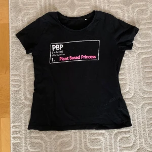 Svart t-shirt med texten 'Plant Based Princess' - Säljer en svart t-shirt med trycket 'PBP Plant Based Princess' i vitt och rosa. T-shirten har en normal passform och korta ärmar. 