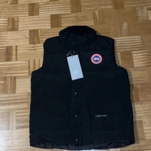 Svart dunväst från Canada Goose - Jag säljer en äkta Canada Goose-väst i utmärkt skick. Den är perfekt för kalla dagar och har en stilren design som passar både till vardags och mer avslappnade tillfällen. Jag tar gärna emot byte!