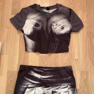 Snygg kortkjol i svart och vitt med ett unikt tryck. Kjolen har en modern design med veckdetaljer framtill. Perfekt för dig som vill sticka ut med en cool look.