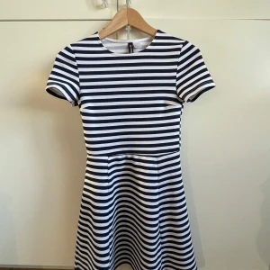 Randig klänning från H&M Divided - Snygg randig klänning,medellång (strax ovanför knäna)  från H&M Divided i marinblått och vitt. Klänningen har korta ärmar och en skön passform.  Perfekt för en avslappnad stil med en touch av elegans. Polyester och elastane. 