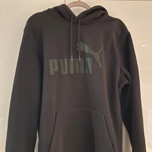 Svart hoodie från Puma - Säljer en stilren svart hoodie från Puma med logga på bröstet. Tröjan är i väldigt bra skick och är nästan aldrig använd då den inte längre passar.