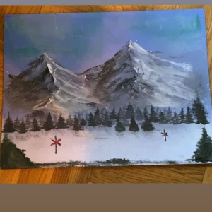 Målning av bergslandskap - En vacker målning som föreställer ett bergslandskap med snötäckta toppar och en skog av granar i förgrunden. Himlen är blå med inslag av lila och grönt, vilket ger en känsla av skymning. Två små röda ledkors syns i snön framför skogen. 40x30 cm🫶🏼