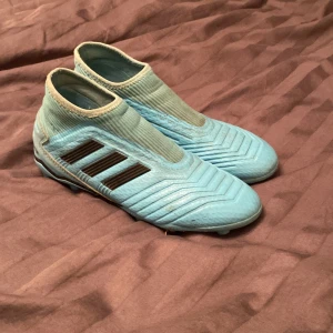 Blå Adidas Predator fotbollsskor - Säljer ett par blå Adidas Predator fotbollsskor med ikoniska tre ränder i svart på sidan. Skorna har en strumpliknande passform utan snörning som är i storlek 37 och 1/3